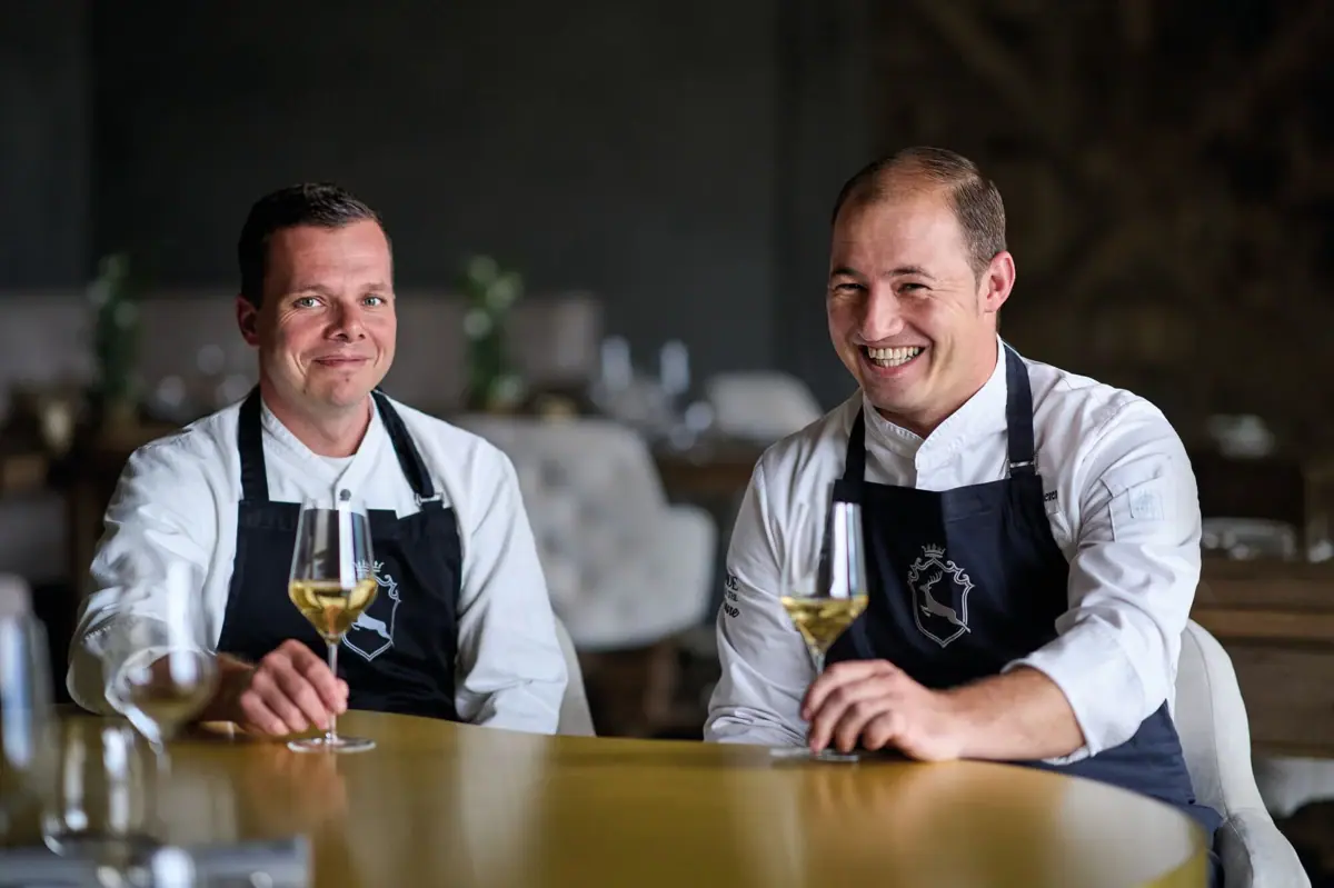 Hans and Sascha at the brass table in the Ifen Hotel Two men in aprons are sitting at a table with glasses of wine.