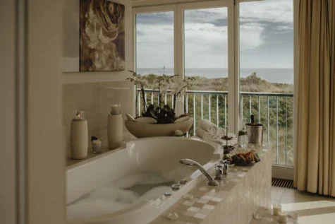 A privat SPA with a filled bath tub and decorations overlooking the beach and sea through a big window. 