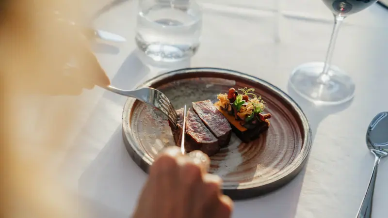 Steak & Wine at the Belvedere Restaurant A person is cutting meat on a plate.
