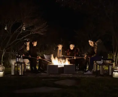 Group of people sitting around an outdoor fireplace at night.