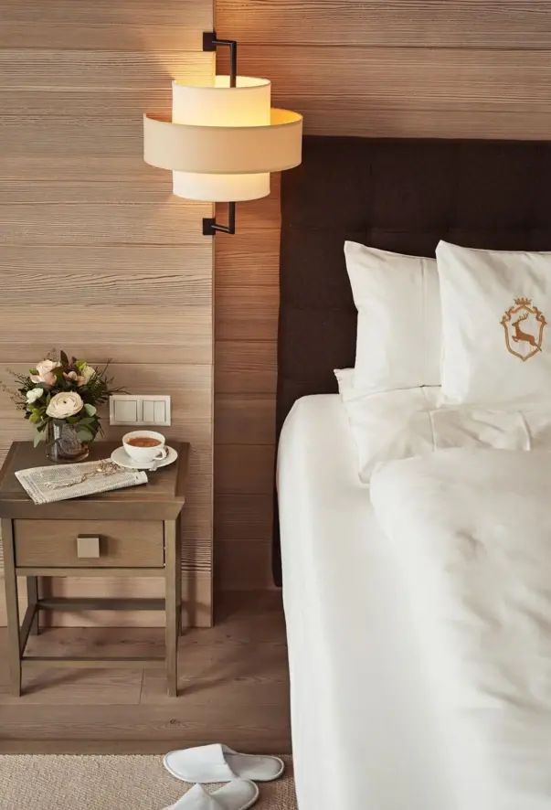 A comfortably furnished bed with a cup of coffee and a vase of flowers on the bedside table.