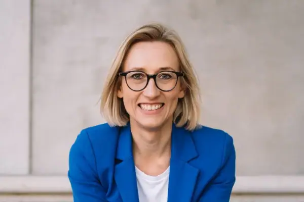 Eine Frau im blauen Anzug sitzt auf Stufen und lächelt.