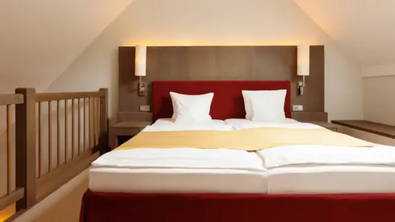 A red upholstered bed stands at the top of a gallery under sloping ceilings.