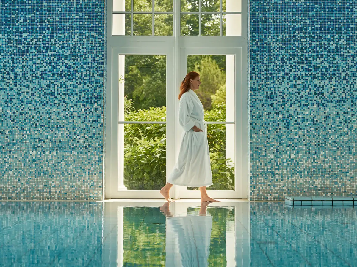 Guest in a bathrobe walking along the poolside at SPA-ROSA wellness area.