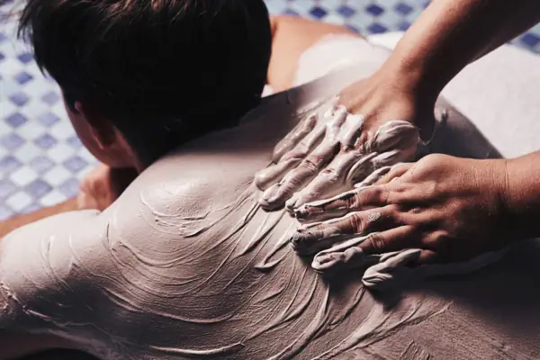 A person's hands applying a white substance on another person's back.