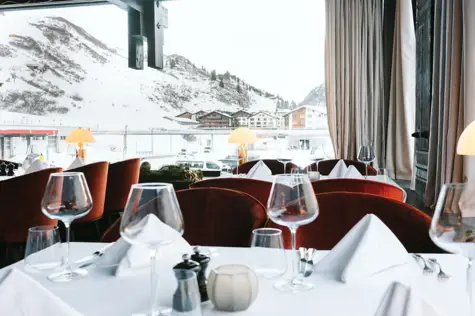 Elegantly set restaurant table with wine glasses and a view of snowy mountains.