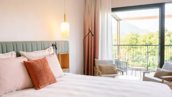 Cozy hotel room with a neatly made bed, plush pillows, and a lamp, leading to a balcony.