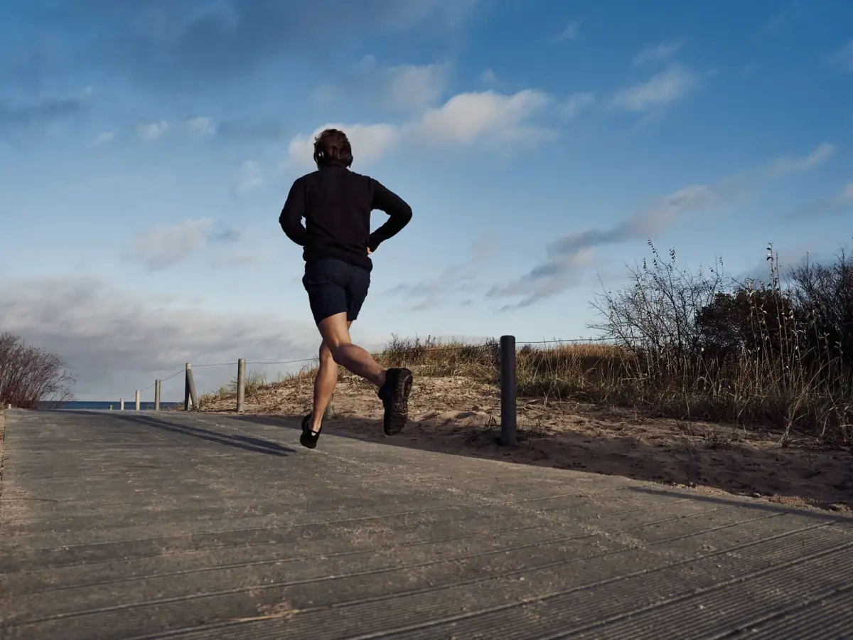 A person running on a path outdoors under a partly cloudy sky.
