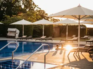 Outdoor pool surrounded by parasols and sun loungers under a blue sky.
