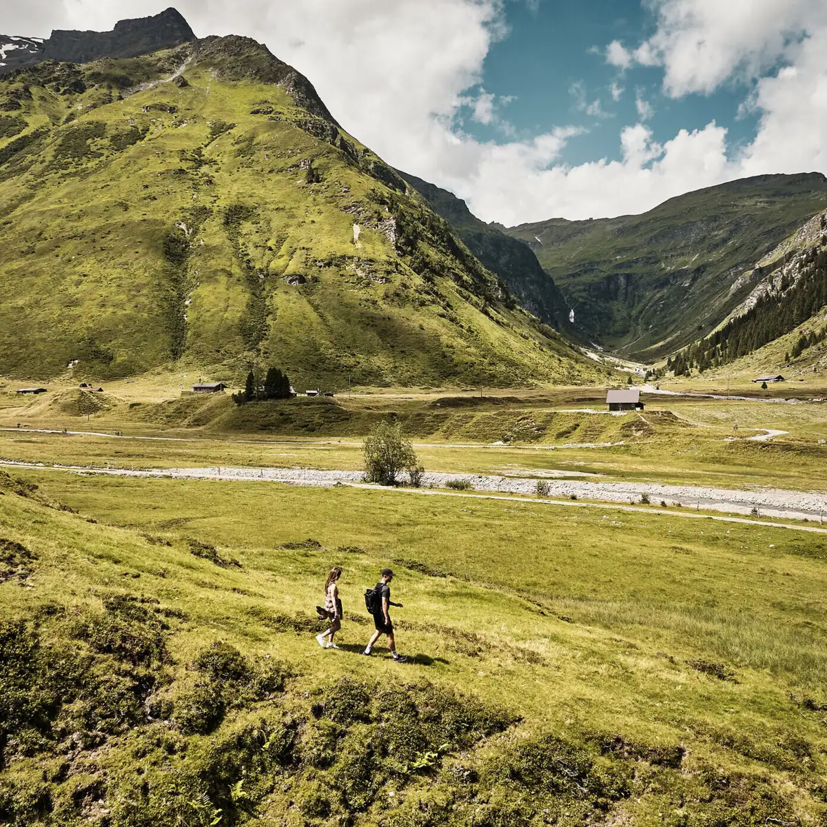 Couple hiking in the Gastein Valley in Salzburger Land with panoramic mountain views and green Alpine meadows in summer.
