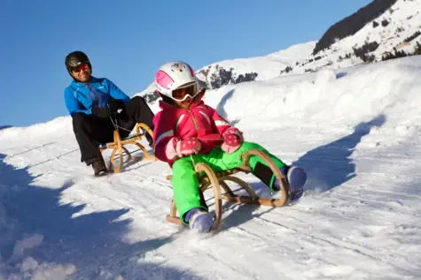 A man and a girl are tobogganing down a snowy slope.