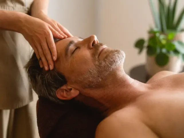 Two hands are massaging the head of a man with closed eyes. 