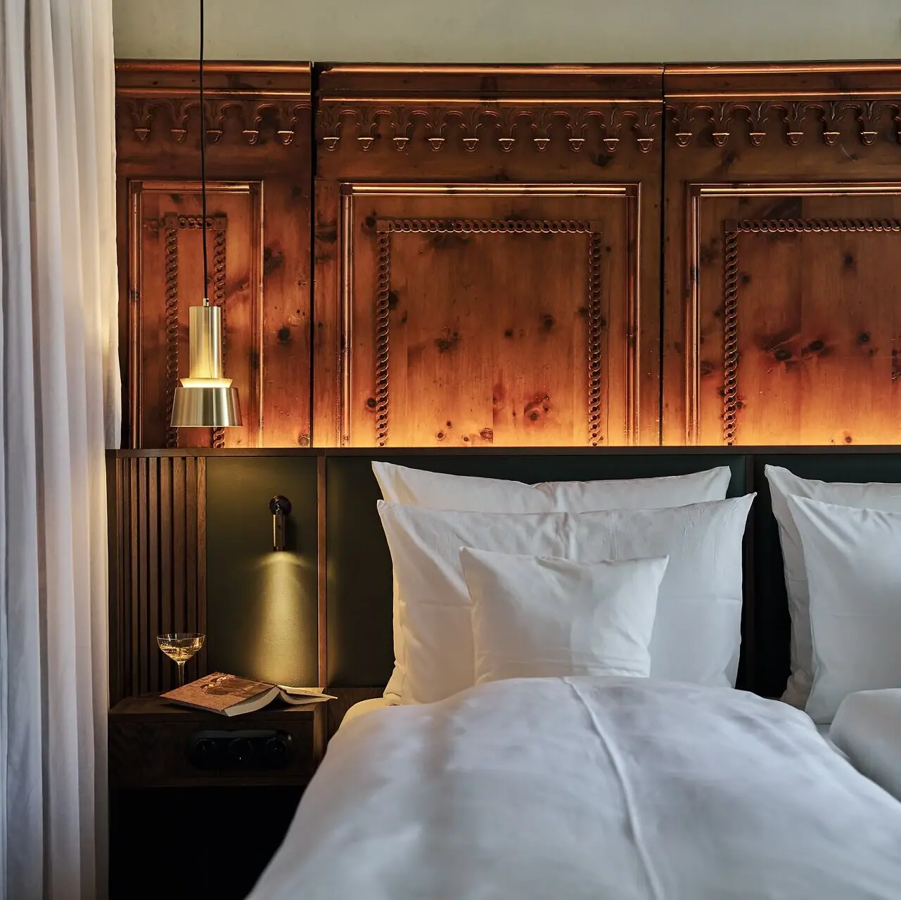 A bed with white pillows and a lamp at the side.