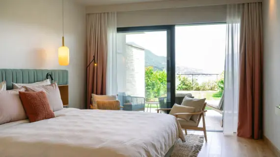 Elegantly designed hotel bedroom featuring a plush bed with multiple pillows, surrounded by several chairs and stylish curtains.