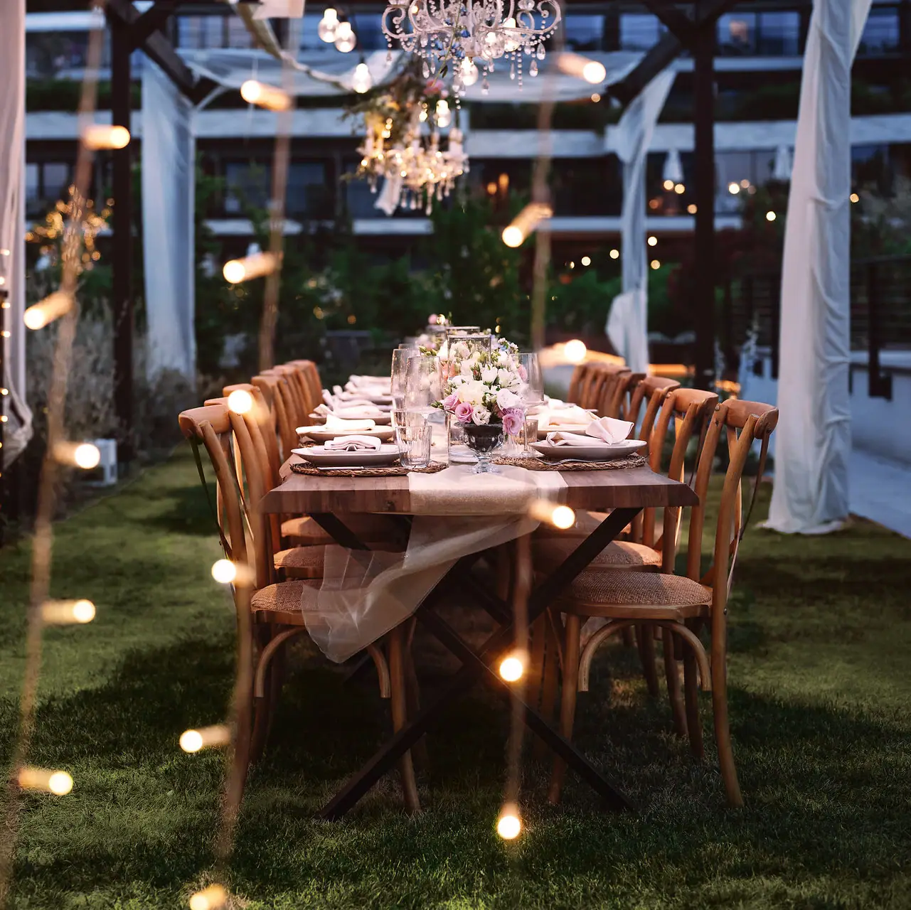 A table set for a dinner party with candles and outdoor lighting.