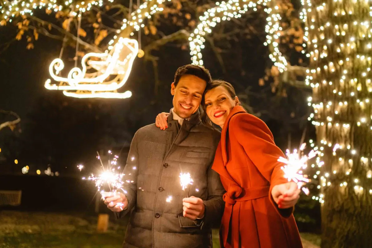 A man and a woman hold sparklers in front of fairy lights.
