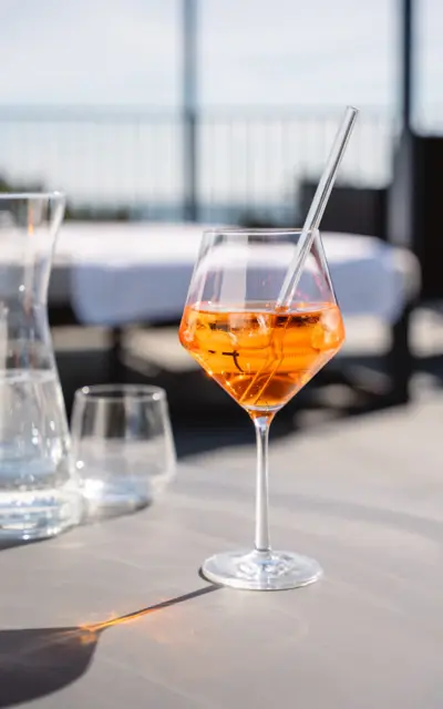 A glass with an orange cocktail and ice cubes on a table.