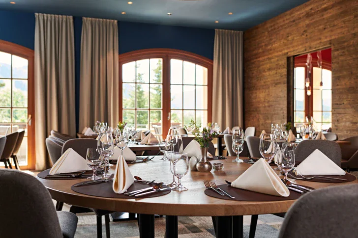 An elegantly set dinner table with tableware, wine glasses, and a vase, in a stylish indoor setting.