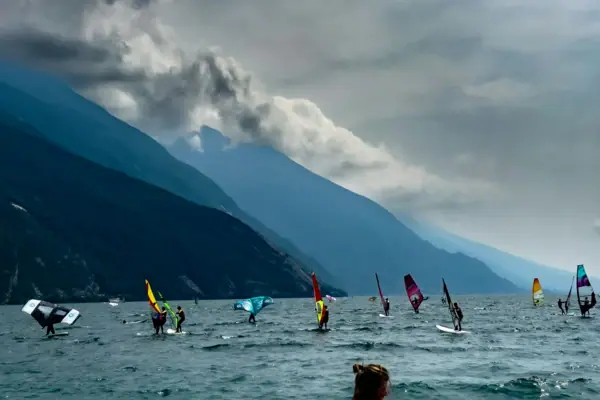 Windsurfers off Torbole A group of people on sailboards on the water, with mountains in the background.