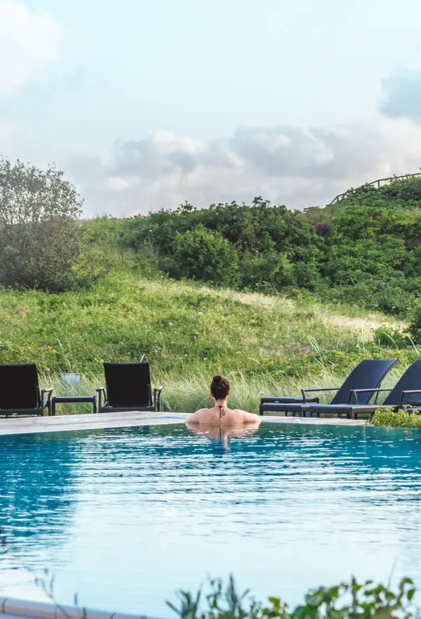 A woman swimming in an outdoor pool surrounded by green fields with small flowers. 