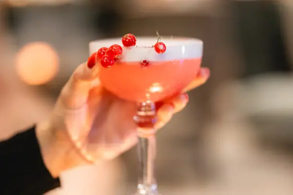 Eine Hand hält ein Glas mit rosa Flüssigkeit.