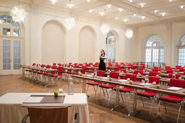 Weißer Saal Ein großer Tagungsraum mit Tischen und roten Stühlen.