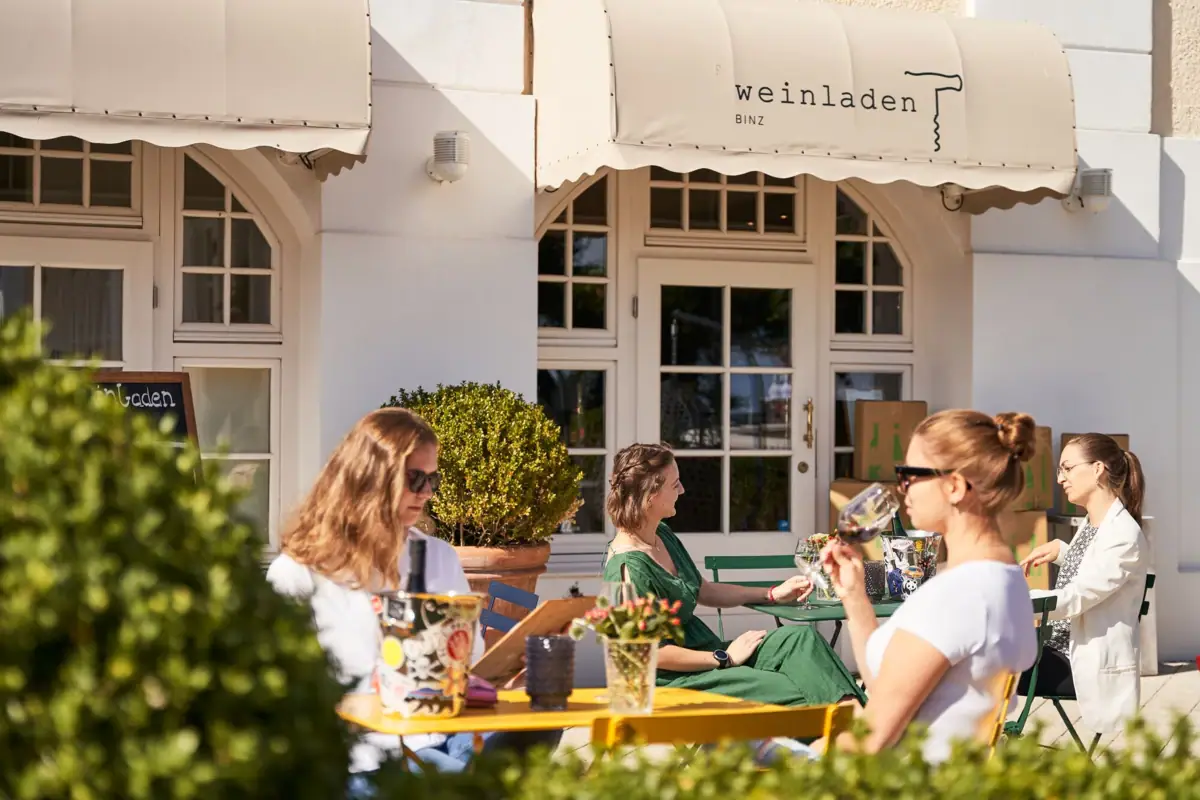 Terrasse Kurhaus Binz Weinladen Eine Gruppe von Frauen sitzt an einem Tisch vor einem Gebäude.