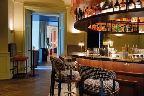 Interior view of a bar with counter, chairs, bottles and shelves.