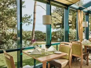 A table with chairs and napkins in a conservatory with a view of the countryside.