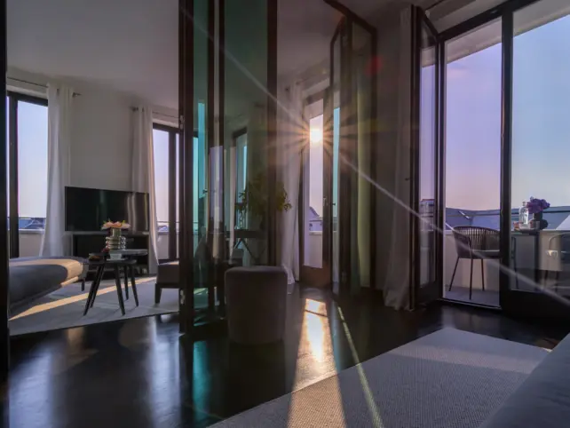 A cozy hotel room featuring a comfortable couch facing a television, with a window providing natural light.