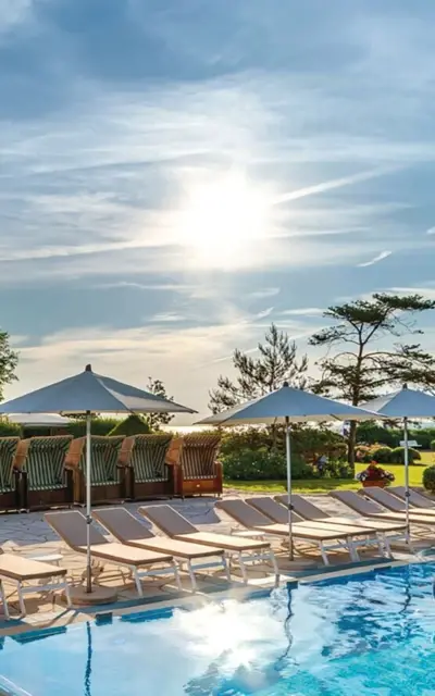 Swimming pool surrounded by lounge chairs and umbrellas under a clear sky.