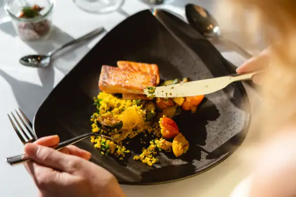 Eine Frau mit blonden Haaren isst mit Messer und Gabel von einem Teller.