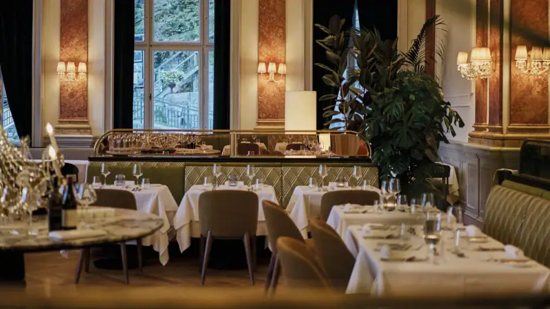 A restaurant interior with tables and chairs near large windows.