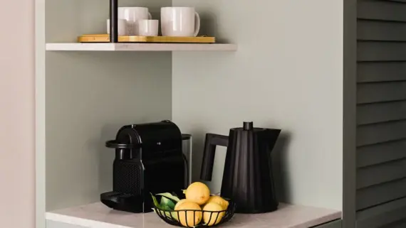 A shelf in a kitchen setting featuring a basket of lemons and a coffee maker.