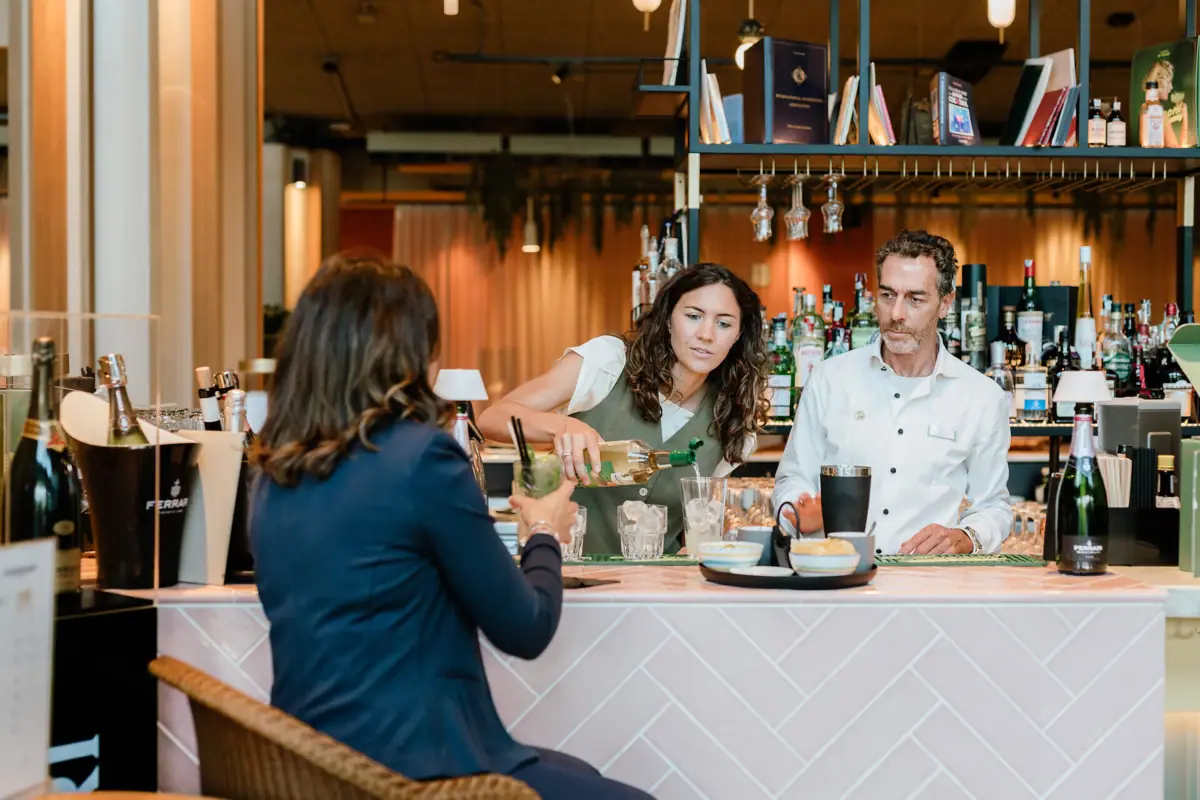 A woman pouring a drink into another woman's glass at a bar.