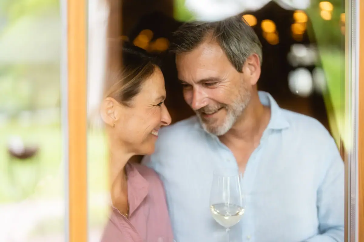Ein Mann und eine Frau schauen sich lächelnd an, beide halten ein Weinglas.