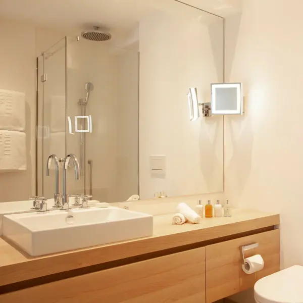 A modern bathroom with a large washbasin made of light-colored wood, on which an angular white washbasin stands. A glazed shower cubicle can be seen in the mirror image.