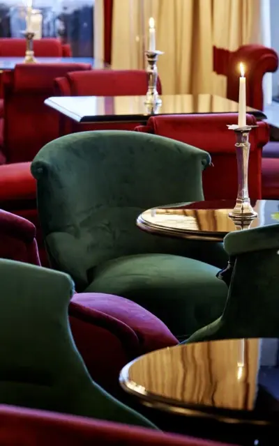 Purple and green armchairs arranged around a coffee table with candles placed on them in an elegantly designed room.