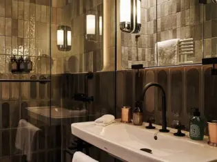 A bathroom with dark, narrow tiles, a shower and a washbasin with a black tap.