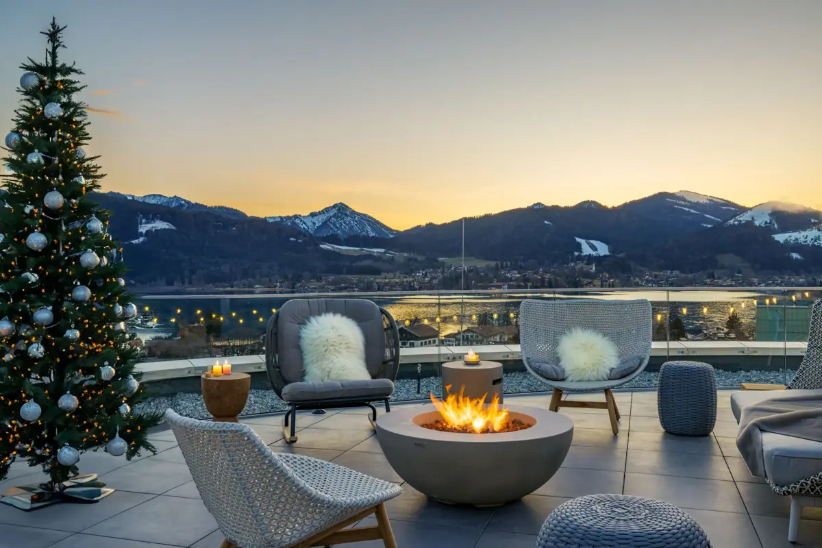 A-ROSA Tegernsee Terrace Christmas The terrace at A-ROSA Tegernsee, featuring a fire pit with chairs and a view of snow-capped mountains in the background.