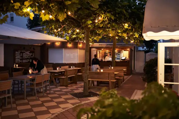 Menschen sitzen an Tischen unter Bäumen im Freien.