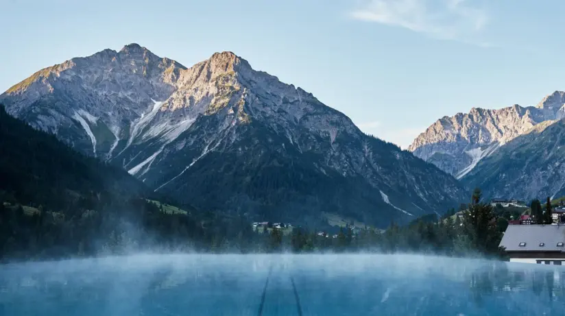 View of an infinity pool in the mountains with snow-capped mountains in the background.