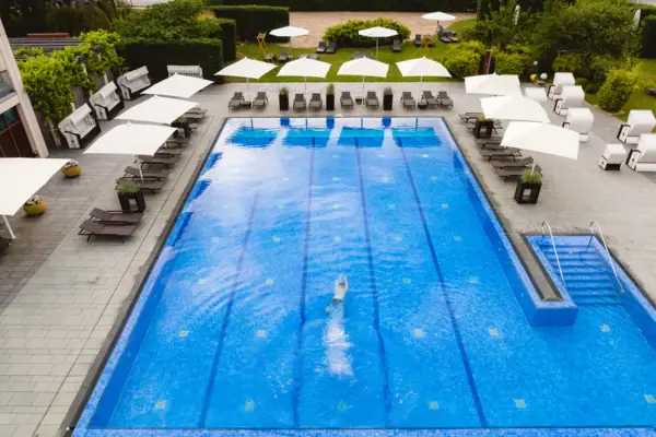 Eine Person schwimmt in einem Außenpool mit Liegen und Sonnenschirmen darum.