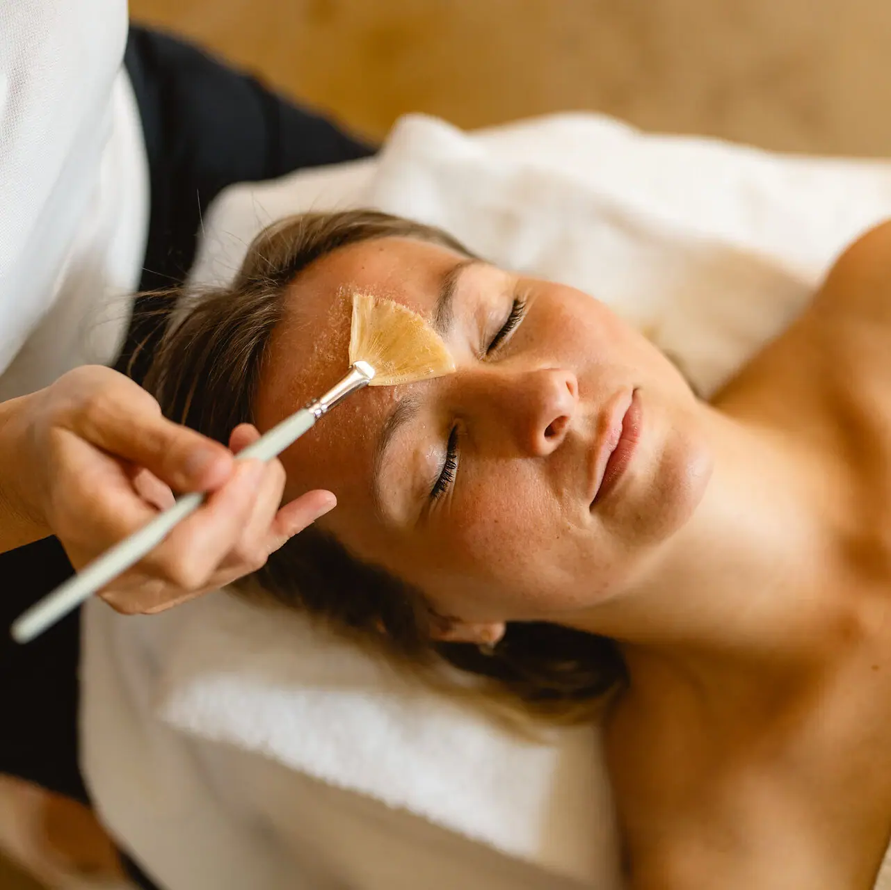 A woman is lying there, relaxed, whilst a brush touches her face.
