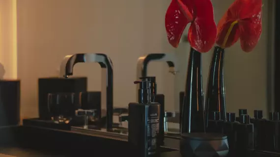 An elegant washbasin in black with a silver tap and a dark vase with a red flower. 