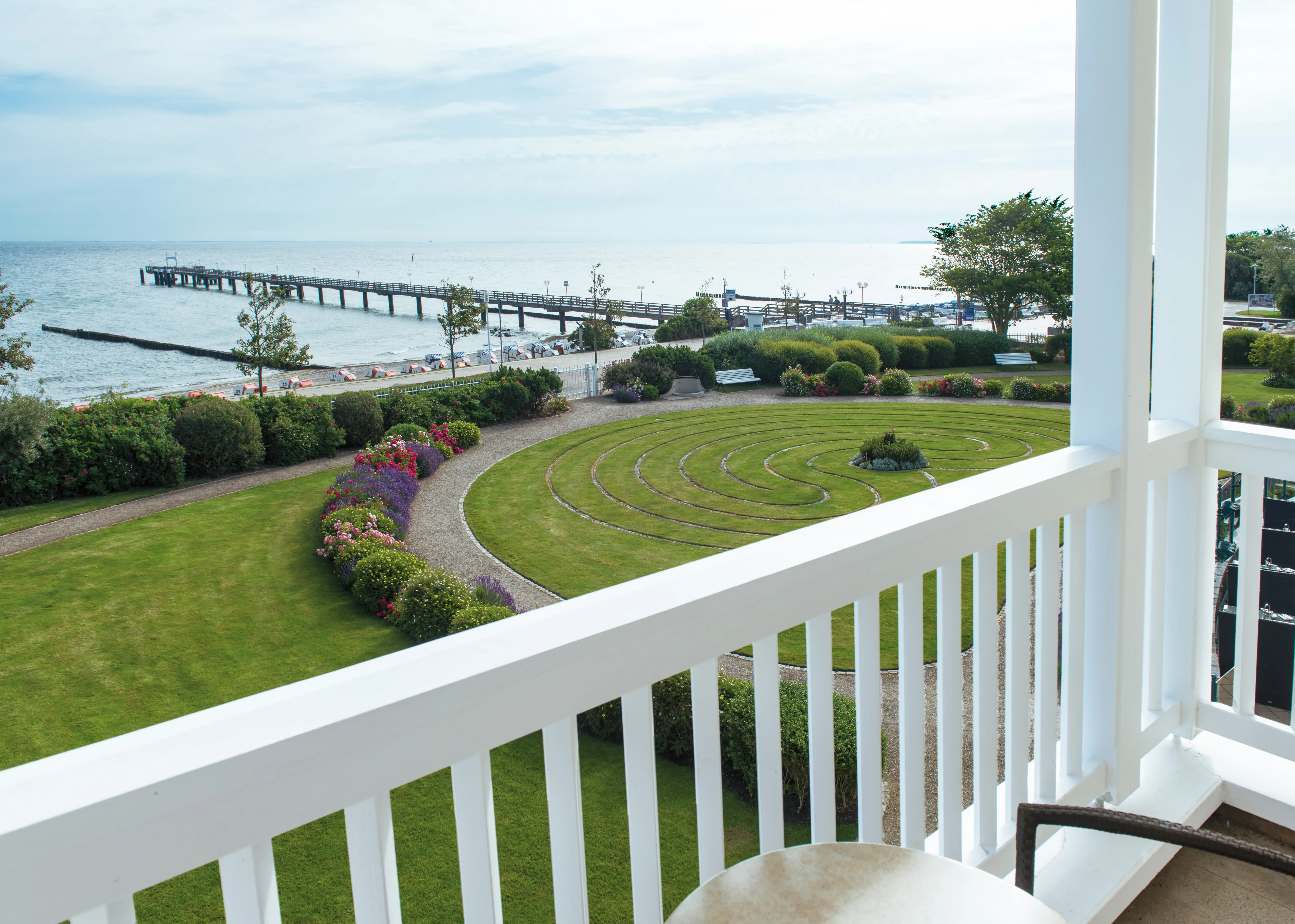 A balcony overlooking a garden and pier with a clear sky.
