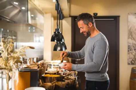 A man stands at a breakfast buffet in a hotel and makes himself a bowl of muesli.