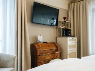 TV mounted on a wall in a well-furnished bedroom with a chest of drawers and bedding visible.