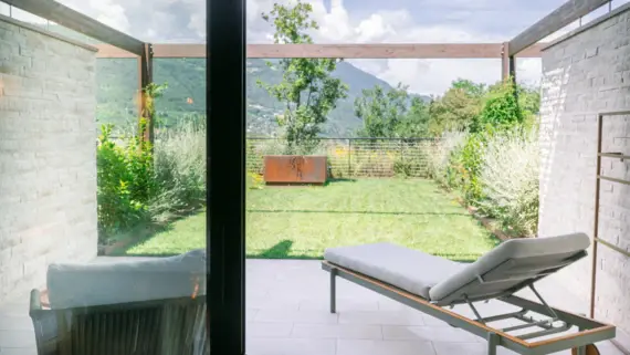 Lounge chair outside with a view of a green yard and mountains, under a cloudy sky.