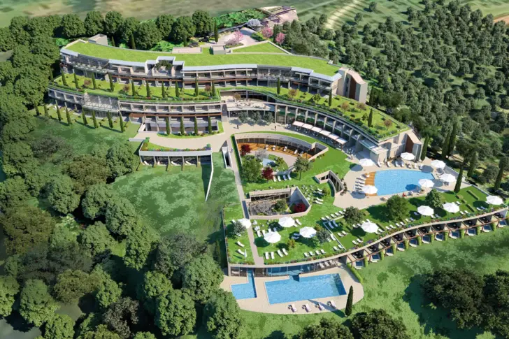 The aerial view of a hotel, which is overgrown with greenery and extends over several levels. In the outdoor area there are pools and sun loungers.